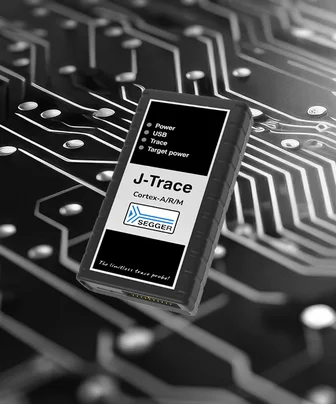 Image of a J-Trace device, featuring a black casing with a label highlighting "Power," "USB," "Trace," and "Target power." The device is placed on a circuit board background, emphasizing its technical purpose. The label also includes "Cortex-A/R/M" and "SEGGER," with a tagline reading "The limitless trace probe.