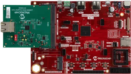 A printed circuit board featuring a red base labeled "SAM9X75-CURIOSITY Rev 5" with various components, including USB ports and connection headers. An attached green board labeled "MICROCHIP" houses an Ethernet port. The layout includes different markings and indicators for connectivity and power.