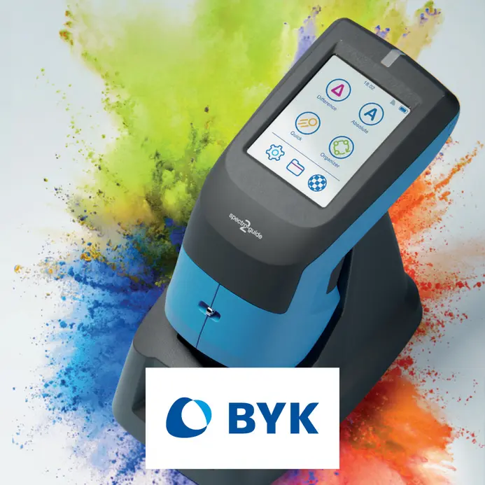 A digital color measurement device is shown, featuring a touchscreen display with icons for various functions. The device is primarily blue and gray, set against a colorful splash backdrop. The BYK logo is prominently displayed below the device.