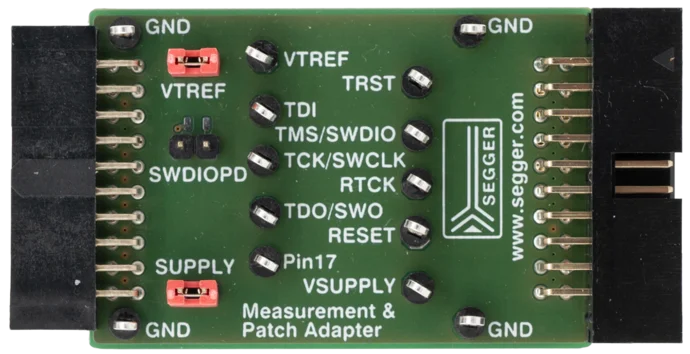A green circuit board featuring various labeled pins and connectors, including GND, VTREF, TDI, and VSUPPLY. The board has red switches and is marked with "SEGGGER" and additional specifications for use as a measurement and patch adapter.
