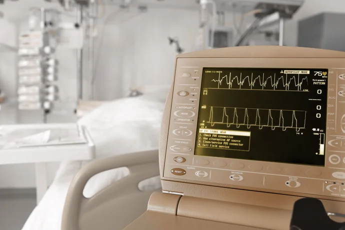 A medical monitor displays a heart rate graph with numerical data, including a heart rate of 75 beats per minute. An alert message prompts the user to check connections and call for service. In the background, a hospital bed and medical equipment are visible.