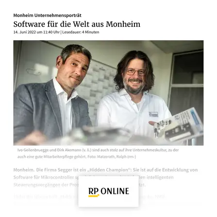 Two men are smiling in an office environment. They are identified as Ivo Geilenbruegge and Dirk Akemann, showcasing their pride in their company culture. In the background, there is a chart or display likely related to technology. The image emphasizes their collaboration in software development for microcontrollers.