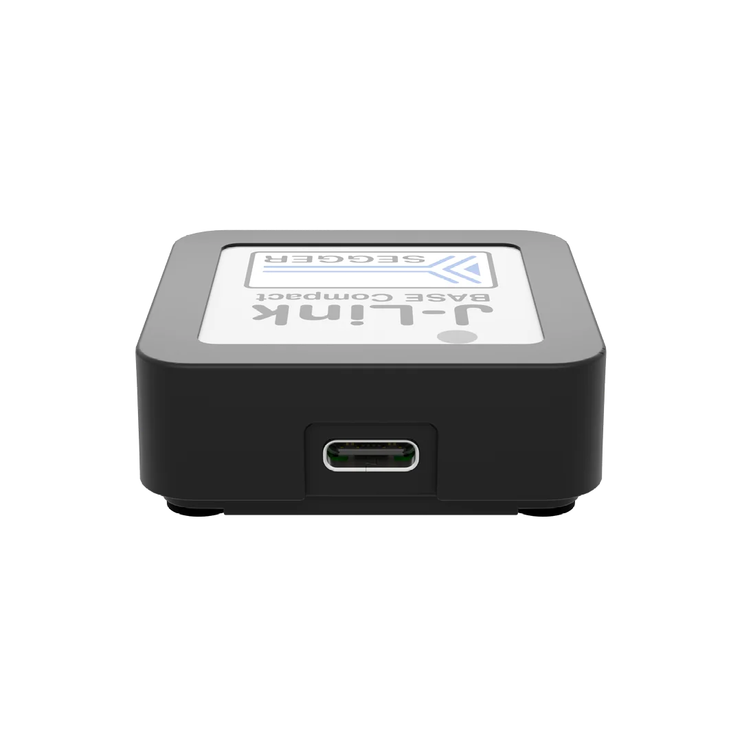 A compact electronic device with a flat, square body featuring a label that reads "J-Link Base Compact" and the logo of the manufacturer, Segger. The device has a USB-C port on one side for connectivity.