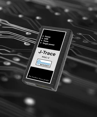 A J-Trace RISC-V debugging device with a black casing and a white label, positioned on a background of circuit board patterns. The label displays icons for power, USB, trace, and target power, along with the SEGGER logo and the phrase "The limitless trace probe.