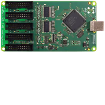 A top-down view of a green circuit board featuring multiple connector pins, integrated circuits, and a USB port on the right side. The board is labeled "emControl I/O" and includes various electronic components typical of a microcontroller interface.