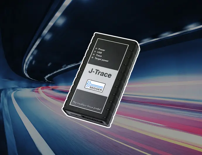Image of a J-Trace device by SEGGER, a black rectangular box with labeled buttons for power, USB, trace, and target power. The device is displayed against a blurred background of dynamic light trails, suggesting motion and modern technology.