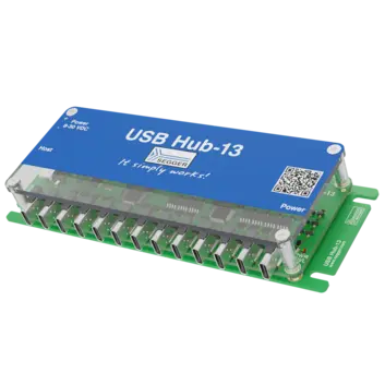 Image of a USB Hub-13 device featuring a blue top panel labeled with "USB Hub-13" and "It simply works!" Above it, the power input specifications are listed. The hub includes numerous USB ports on its side and is mounted on a green circuit board.