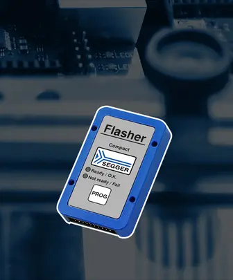 A compact blue device labeled "Flasher" by SEGGER is prominently displayed. The device includes status indicators: "Ready / O.K." and "Not ready / Fail," along with a "PROG" button. The background features a blurred circuit board to indicate its technological context.