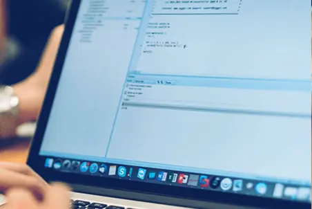 A close-up view of a laptop screen displaying code in a programming environment. A person's hands are partially visible, interacting with the computer. The focus is on lines of code and a text editor interface.