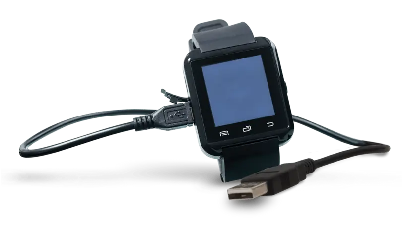 A smartwatch is displayed on a charging dock, connected by a USB cable. The watch features a blank screen and buttons on its front. The charging setup indicates it is in the process of recharging.