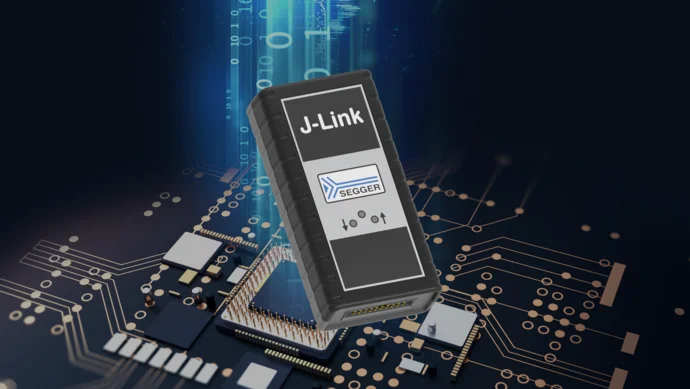 A J-Link device with a SEGGER logo is centered against a dark background featuring a circuit board with various electronic components. The device displays connection ports and buttons, emphasizing its role in programming and debugging embedded systems.