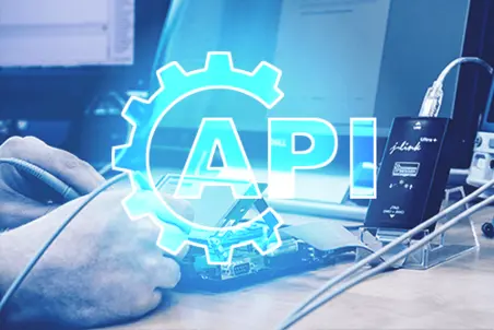 A person is using a pen to interact with a laptop, which is connected to an interface device. Prominently displayed is the term "API," surrounded by a gear icon, suggesting a focus on software integration or development.