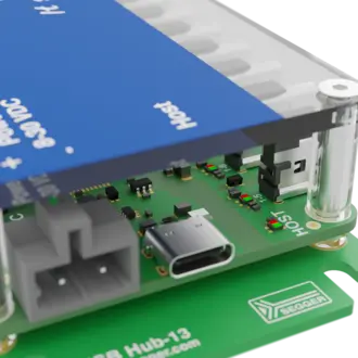 A close-up view of a circuit board featuring a blue component labeled "Host" on top. The board includes various electronic components, connectors, and a USB-C port. It is marked with other small labels and has a green base, suggesting it's part of a device or hub system.