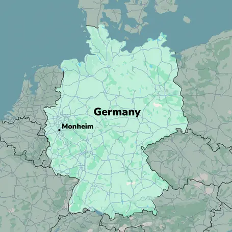 A map of Germany, highlighted in light green, with major roadways marked. The city of Monheim is labeled prominently in black text, located toward the western part of the map. The background features neighboring countries and geographic outlines.