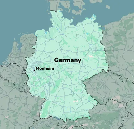 A map of Germany, highlighted in light green, with major roadways marked. The city of Monheim is labeled prominently in black text, located toward the western part of the map. The background features neighboring countries and geographic outlines.