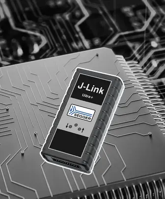 The image features a J-Link Ultra+ programming tool, prominently displayed against a circuit board background. The device has a sleek, black design with a white label displaying the logo "SEGGER" and control symbols, showcasing its role in electronics programming and debugging.