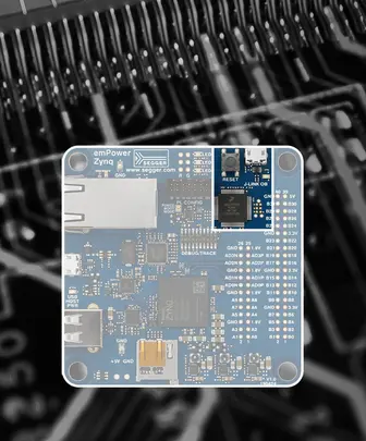 A blue circuit board identified as "emPower Zynq" featuring various electronic components, ports, and labels. The board is central in the image against a blurred dark background, highlighting its design and connections.