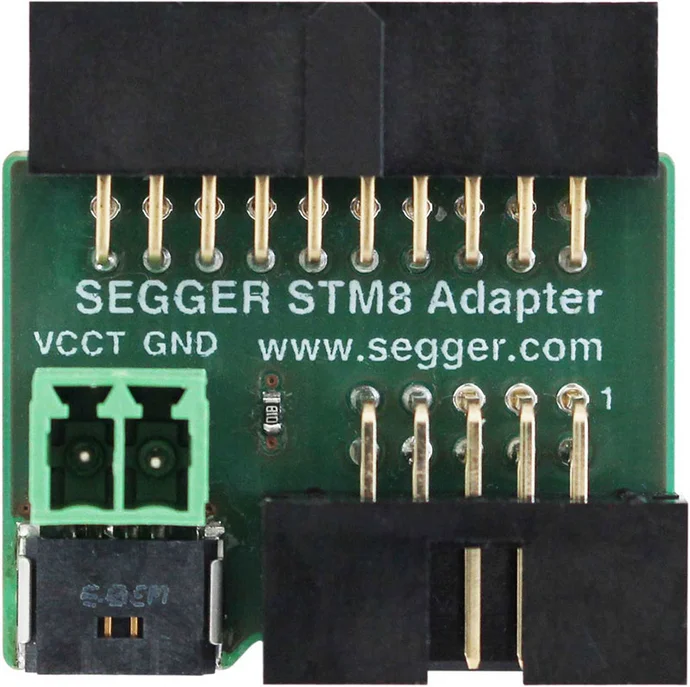 Image of a SEGGER STM8 Adapter, a small green circuit board with multiple gold pins. It features labels for "VCCT," "GND," and a website link. The design includes two terminal blocks and a connector for easy interface with other devices.